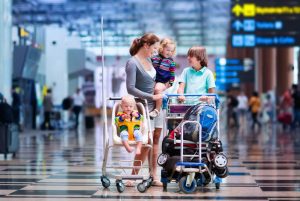 Family traveling with kids. Parents with children at international airport with luggage in a cart. Mother holding baby, toddler girl and boy flying by airplane. Travel with child for summer vacation.